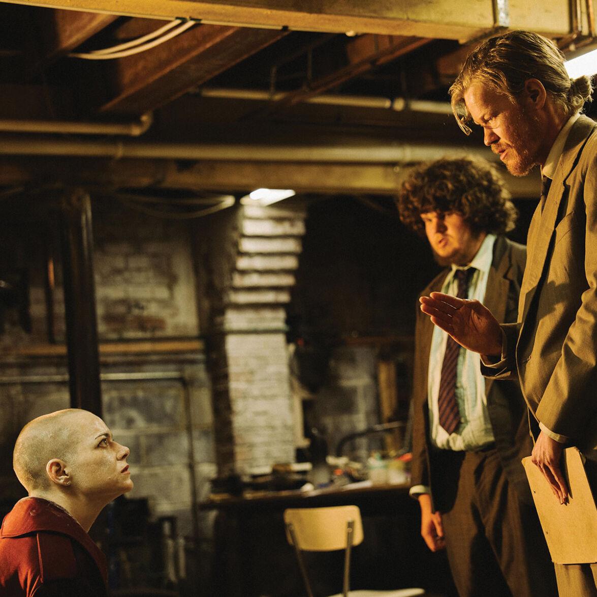 A still from Bugonia with Emma Stone, seated, looking up at Jesse Plemmons.